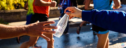Žena podává běžci při maratonu láhev vody.