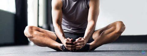 Muž sedí a drží si nohy, aby si protáhl třísla.