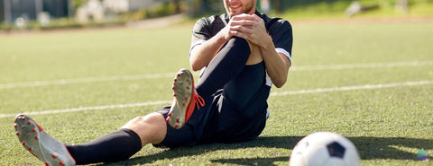 Fotbalista sedí na zemi a drží se za levé koleno.