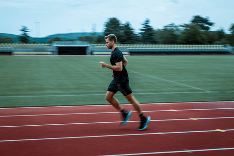Atlet při tréninku běžeckých intervalů na atletické dráze u fotbalového stadionu.