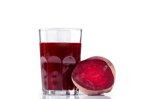 Sklenice s vymačkanou šťávou z červené řepy, rozpůlená červená řepa vedle