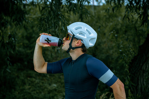 Cyklista v bílé helmě pije předtréninkový nápoj hyve endurance pro.