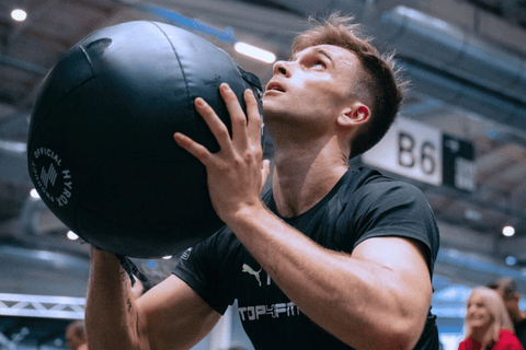Detailní záběr na sportovce při cvičení s medicinbalem na soutěži HYROX.