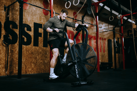 Sportovec během funkčního hyrox tréninku na airbike v posilovně.