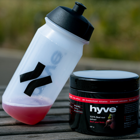 hyve 100% extrakt z červené řepy a bidon s rozmíchaným nápojem z červené řepy na dřevěném stole venku