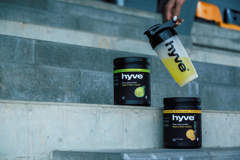 Produkty hyve clear whey protein citron– ananas a limetka a shaker s nápojem položené na schodech stadionu