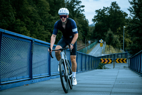 Cyklista na silničním kole stoupá po lávce, v pozadí cyklostezka a zeleň