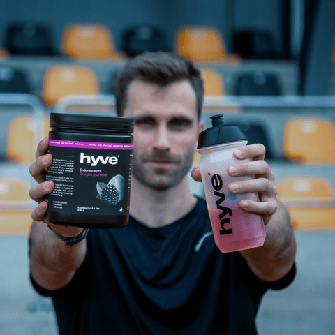 Sportovec na stadionu drží hyve Endurance Pro Blackberry & Lime a shaker s namíchaným nápojem