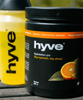 hyve hydration pro s příchutí pomeranče a bidon s rozmíchaným nápojem na venkovním dřevěném stole