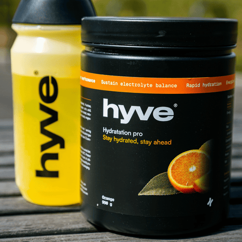 hyve hydration pro s příchutí pomeranče a bidon s rozmíchaným nápojem na venkovním dřevěném stole
