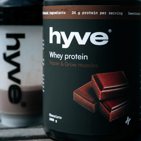 hyve Whey Protein čokoláda a shaker s čokoládovým proteinovým nápojem na venkovním stole