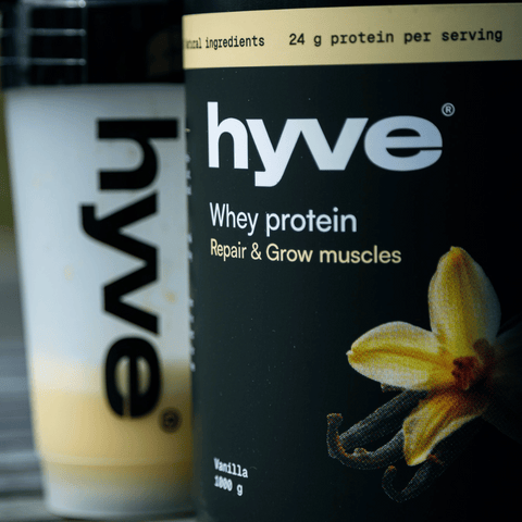 hyve Whey Protein Vanilla a shaker s vanilkovým proteinovým nápojem na venkovním stole