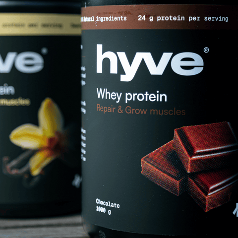 hyve Whey Protein Vanilla a hyve Whey protein Chocolate na dřevěném stole venku