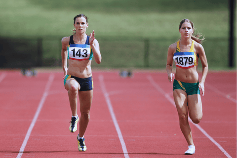 Dvě atletky sprintující na dráze během závodu.