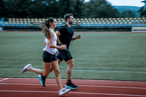 Dvojice běžců v pohybu na stadionové dráze s tribunou v pozadí.