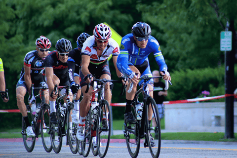 Skupina silničních cyklistů v helmách a dresech závodí po městské trase.