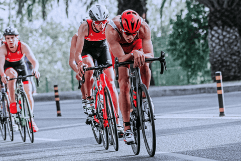 Skupina triatlonistů při cyklistické části závodu na silnici.