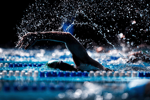 Plavec v bazénu během závodu provádí záběr ve volném stylu, voda stříká kolem.