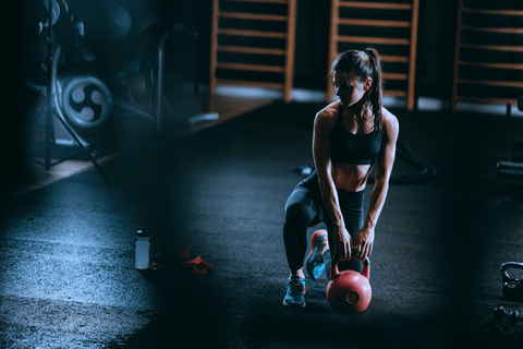 Žena při crossfit tréninku v černém sportovním oblečení se chystá zvednout kettlebell v temnější posilovně.
