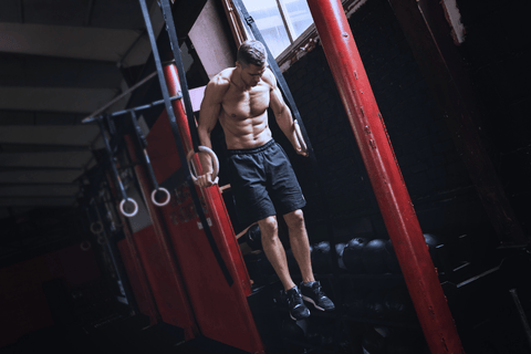 Muž cvičící muscle-up na gymnastických kruzích v gymu.